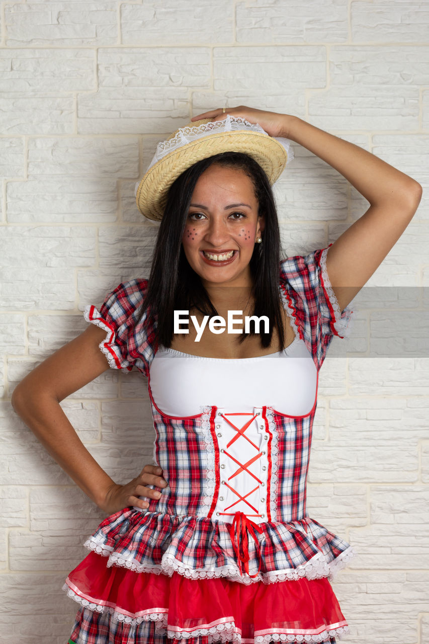 PORTRAIT OF A SMILING YOUNG WOMAN AGAINST WALL