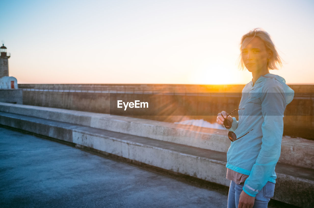 Woman standing on promenade against sky during sunset