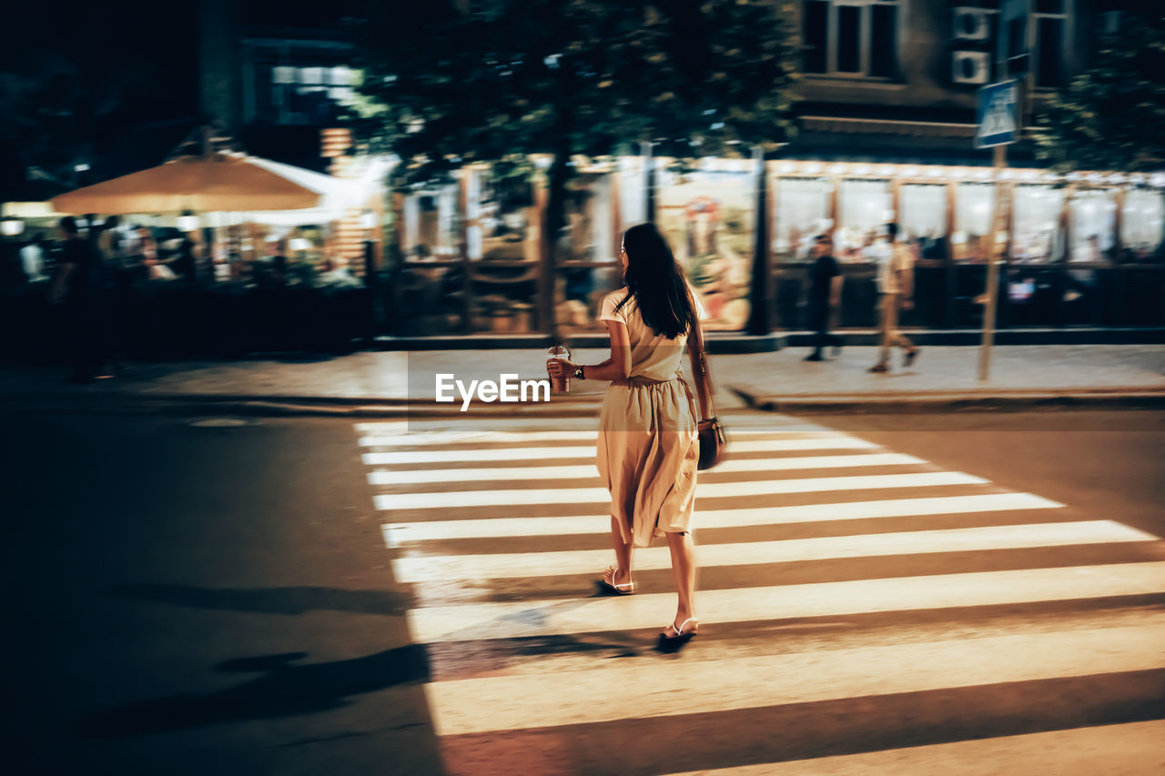 Woman with smoothie crossing street at night