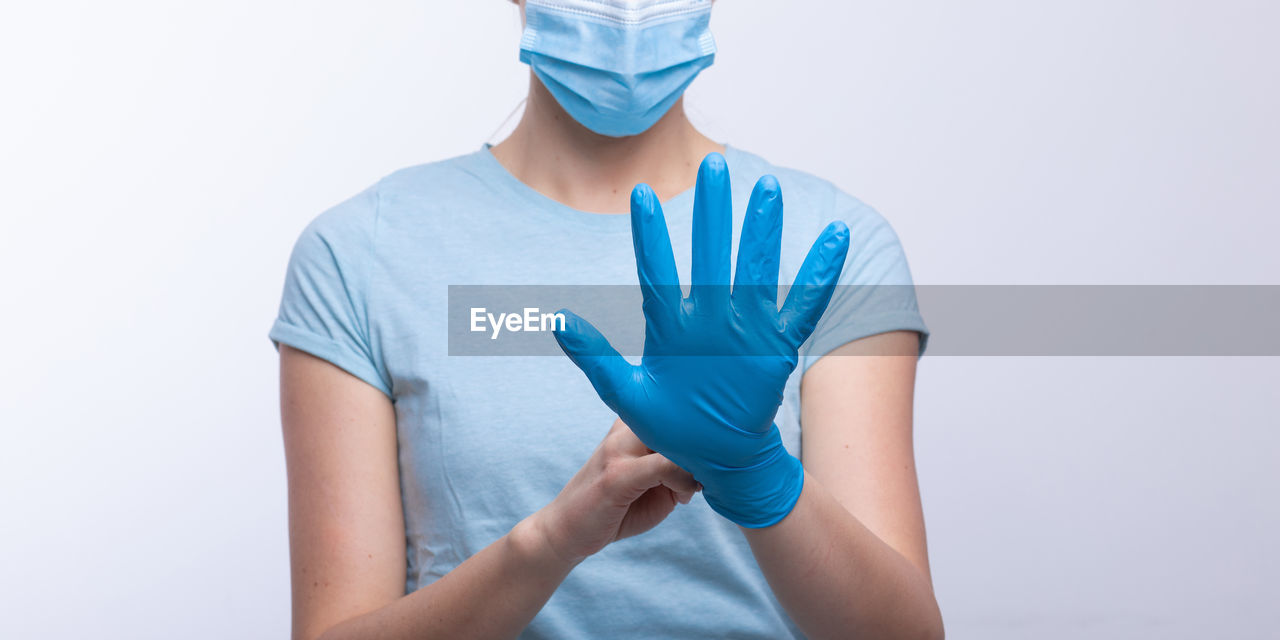 Midsection of doctor in mask wearing surgical glove against gray background