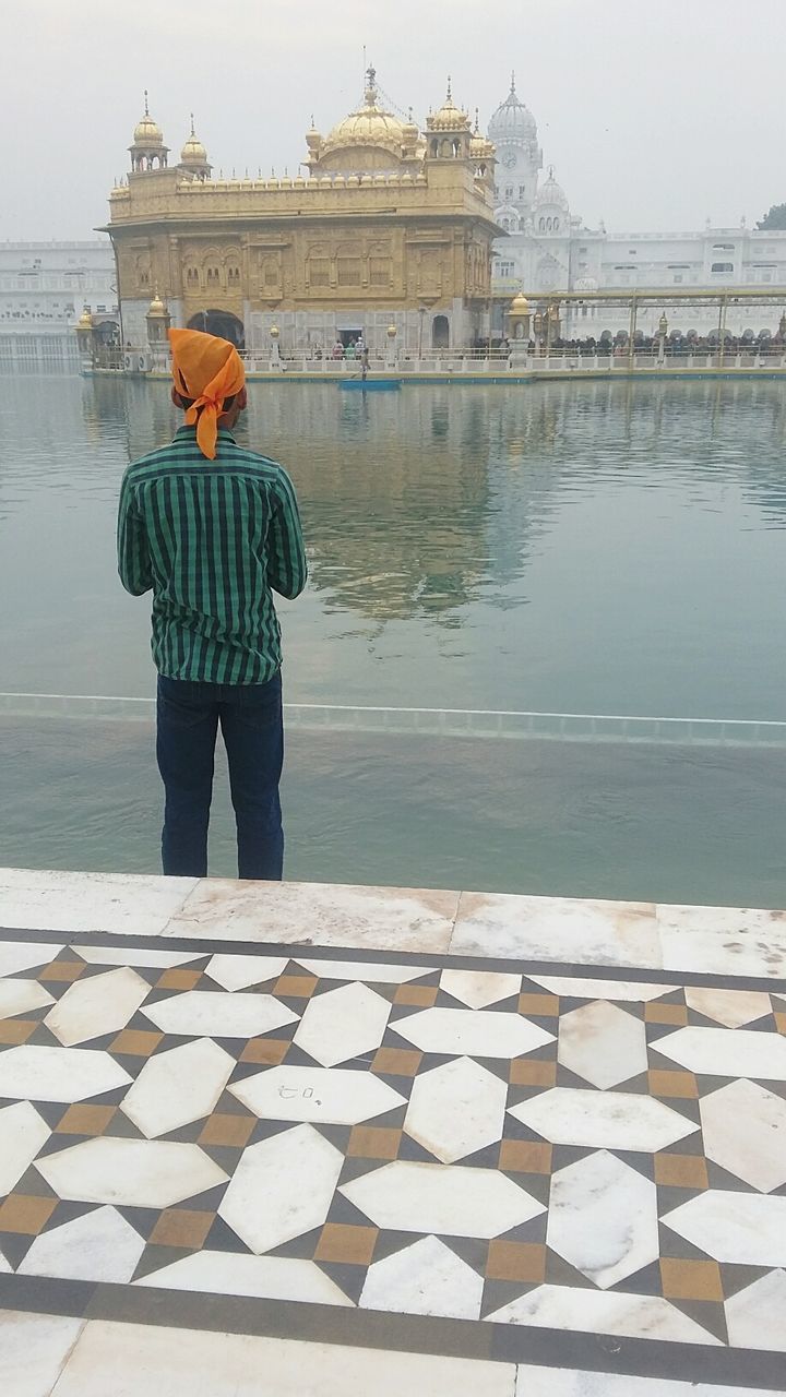 Rear view of man praying by pond at golden temple