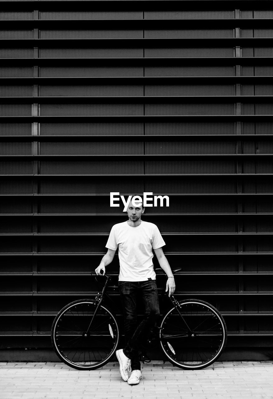 Portrait of young man standing by bicycle against wall