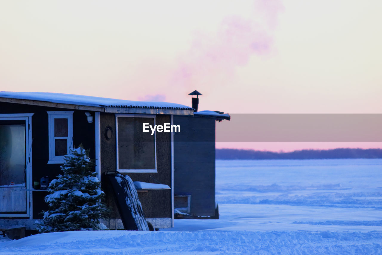 Smoking chimney heating the little ice fishing hut on a frozen lake.