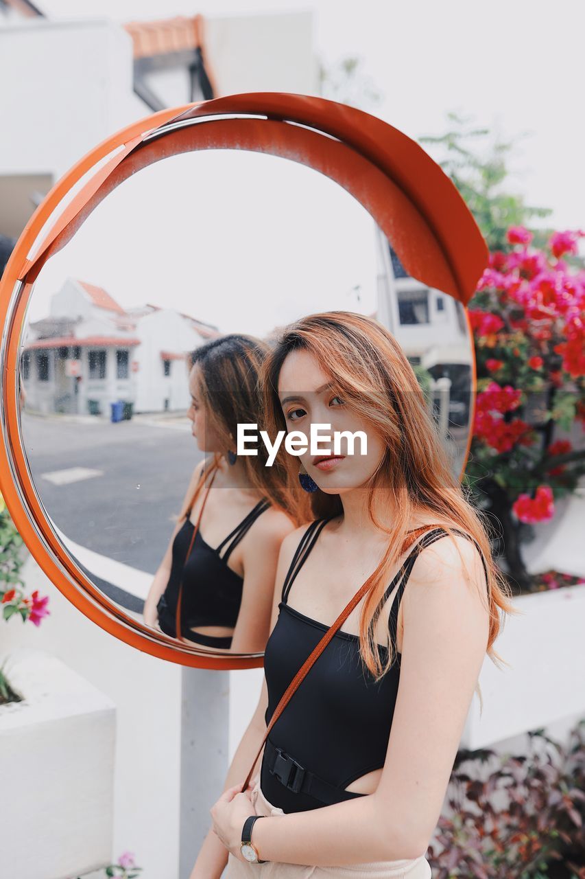 Portrait of beautiful young woman standing by road mirror