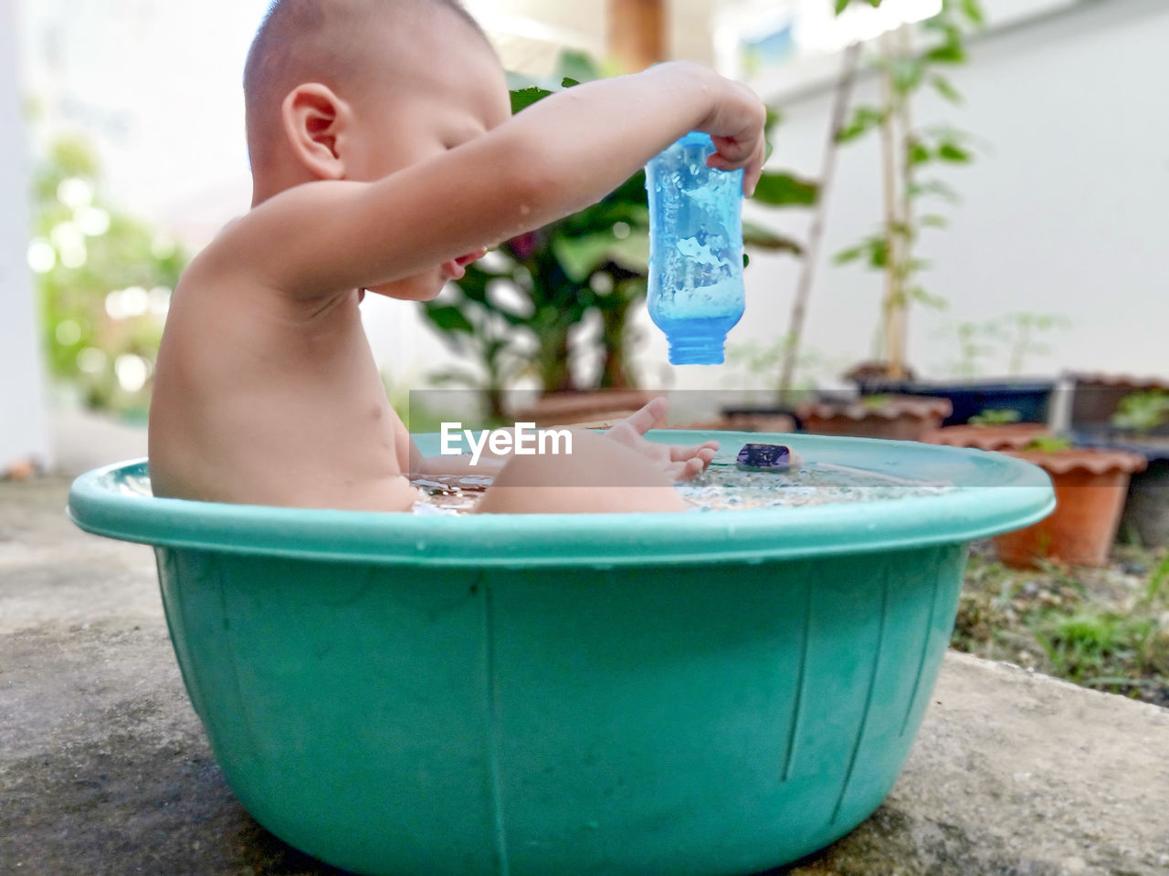 Shirtless boy sitting in container outdoors