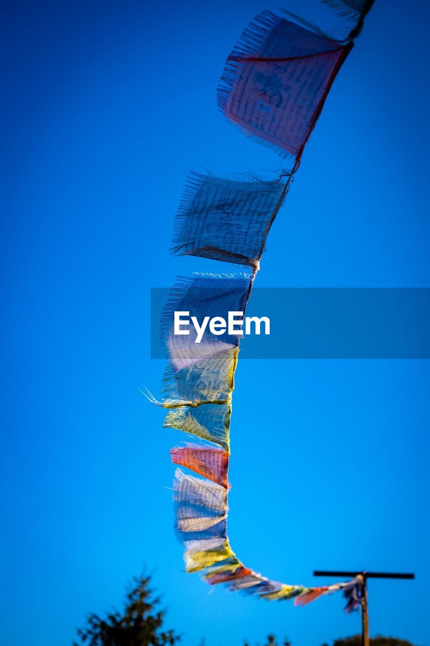 Low angle view of prayer flags hanging against clear blue sky