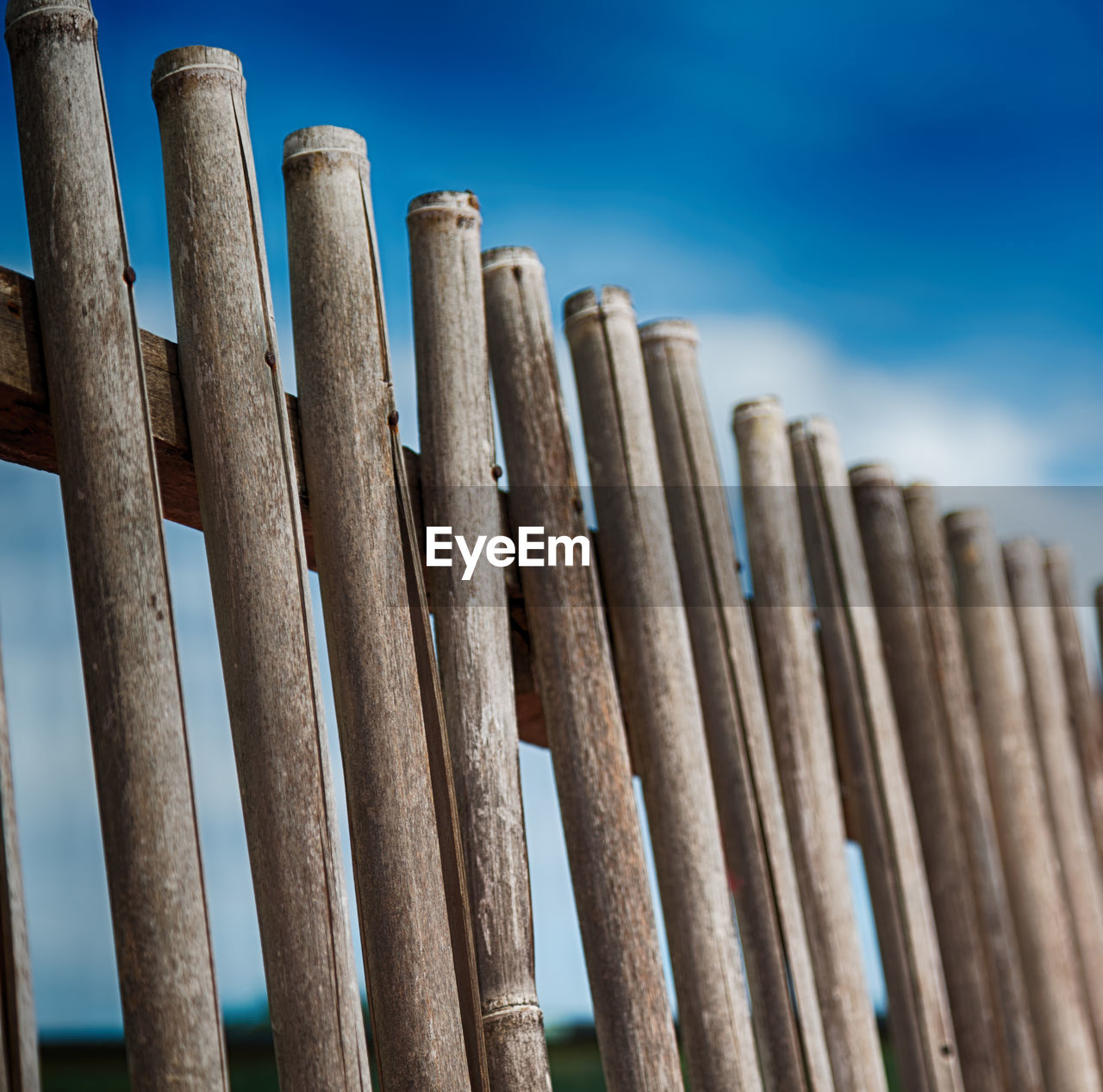LOW ANGLE VIEW OF WOODEN POSTS AGAINST BLUE SKY