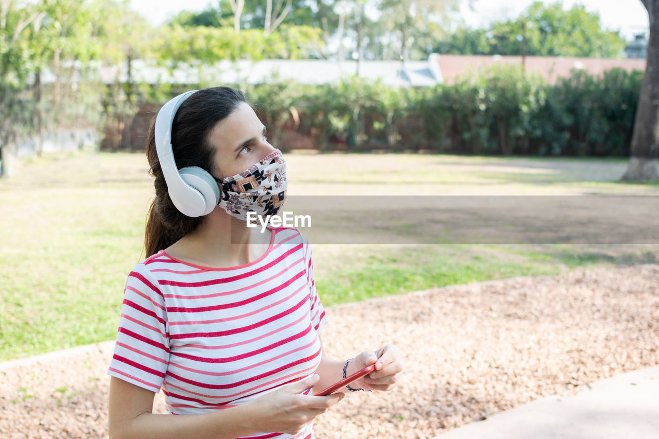 Woman wearing mask looking up whiles standing in park