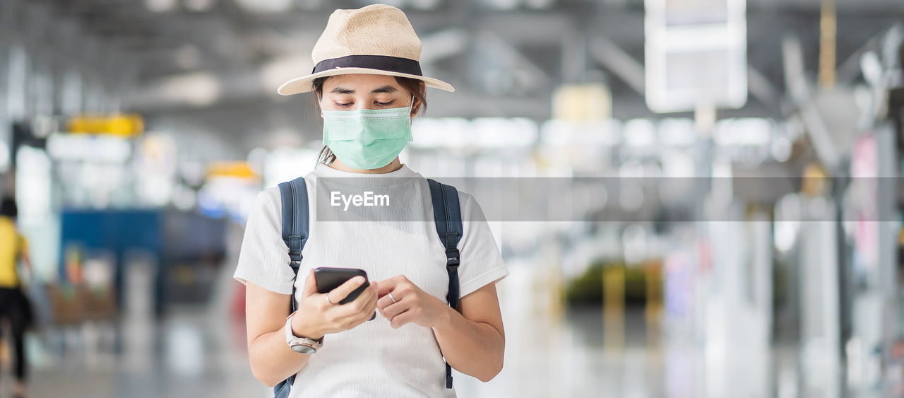 Woman wearing mask using phone standing at airport