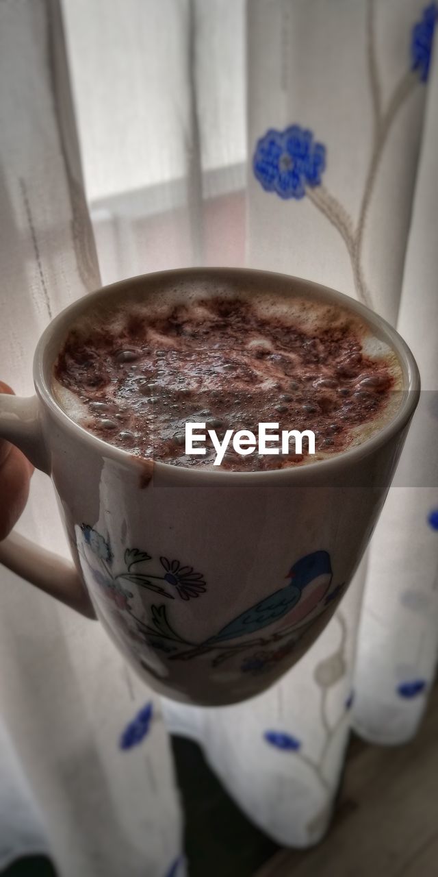 CLOSE-UP OF HAND HOLDING COFFEE CUP WITH SPOON