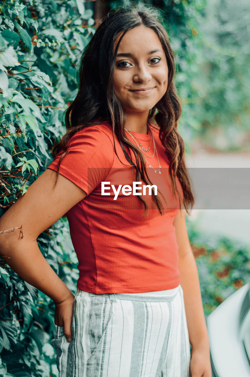 Portrait of a smiling young woman standing by plants outdoors