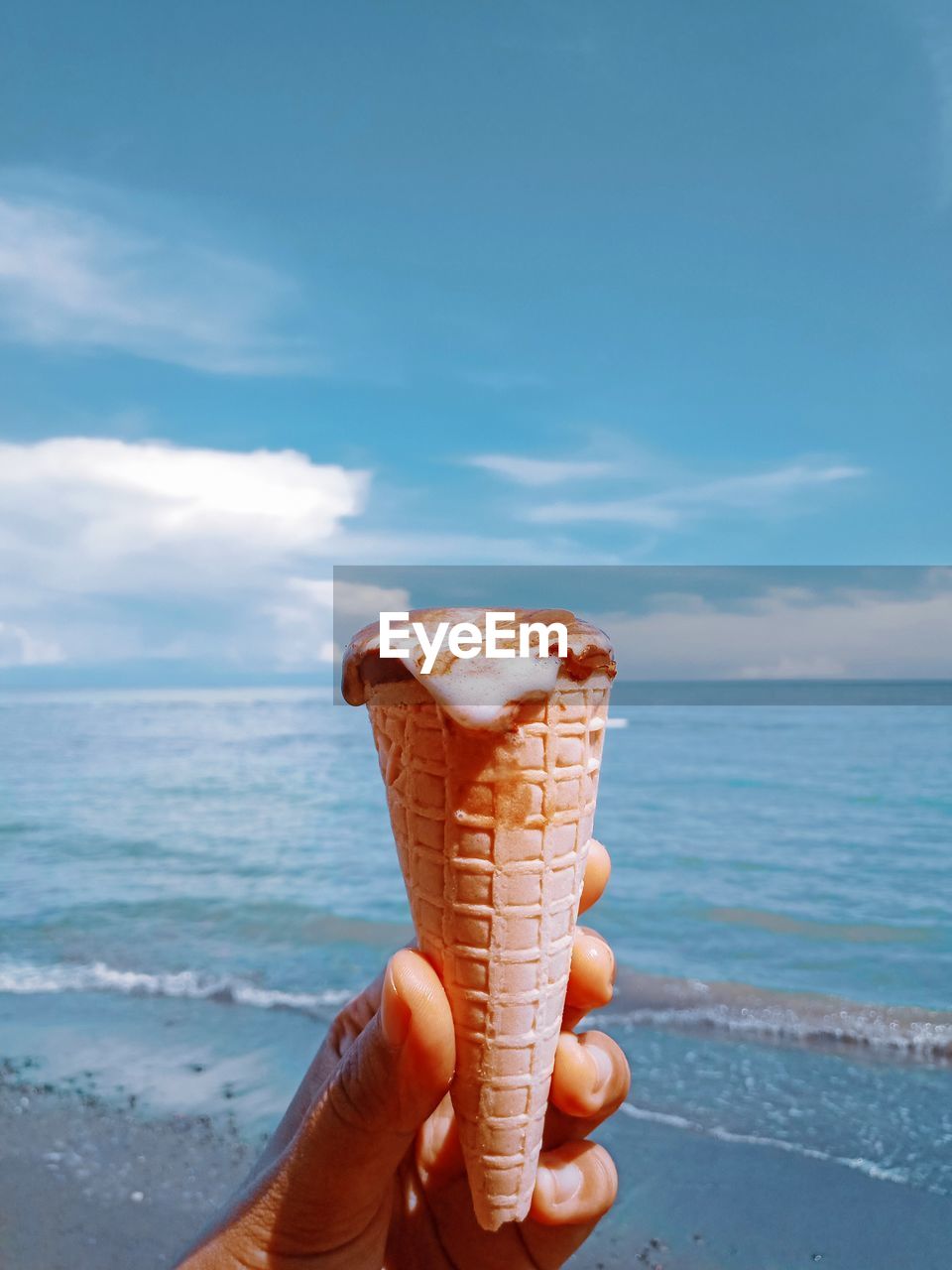 Midsection of person holding ice cream in sea against sky