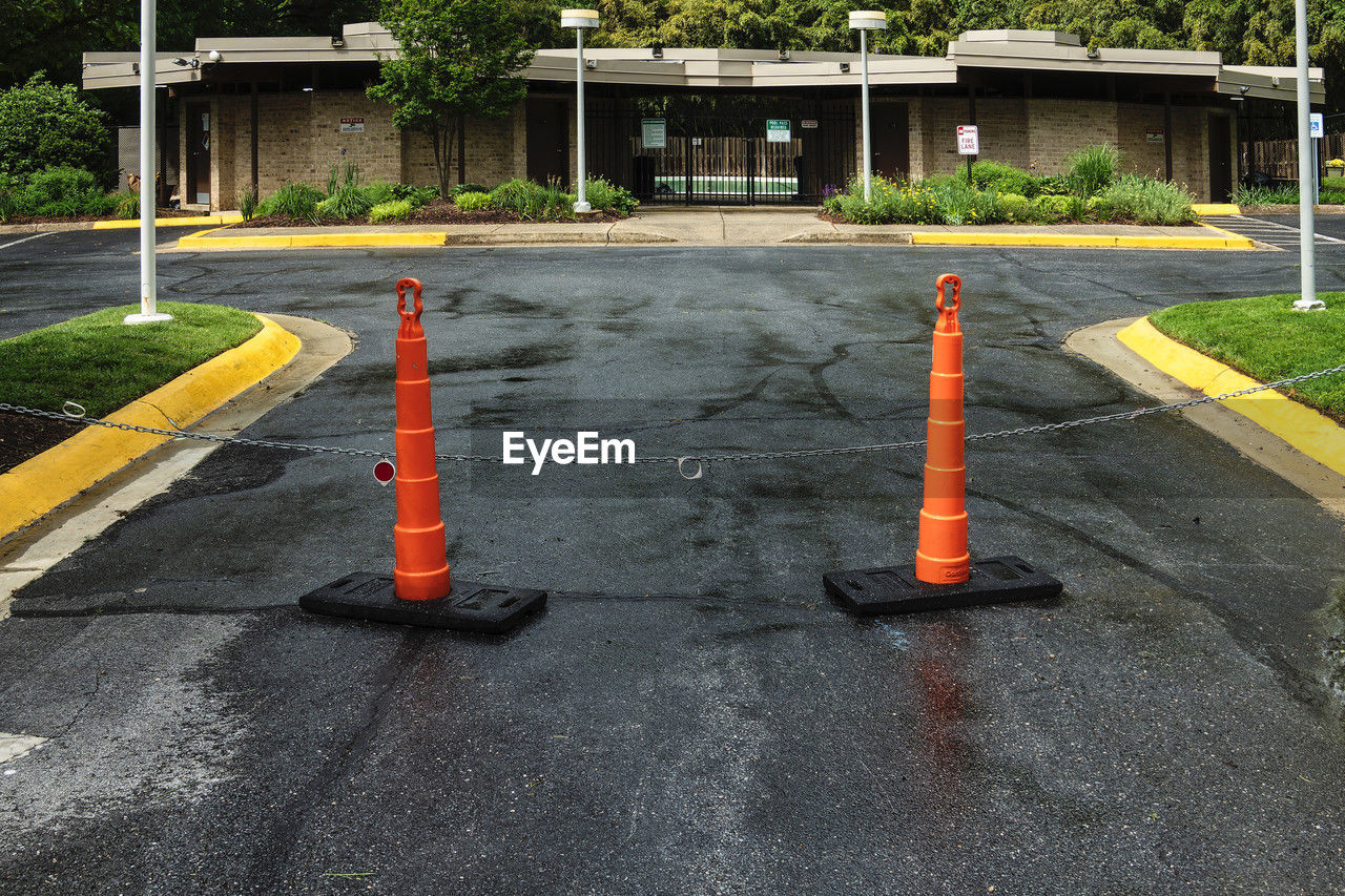 asphalt, traffic cone, cone, road, sign, city, architecture, public space, road surface, no people, built structure, lane, day, transportation, street, outdoors, communication, plant, building exterior, pedestrian crossing, sidewalk, playground, road sign, nature, symbol, road marking, tree, road construction, marking, construction industry, security