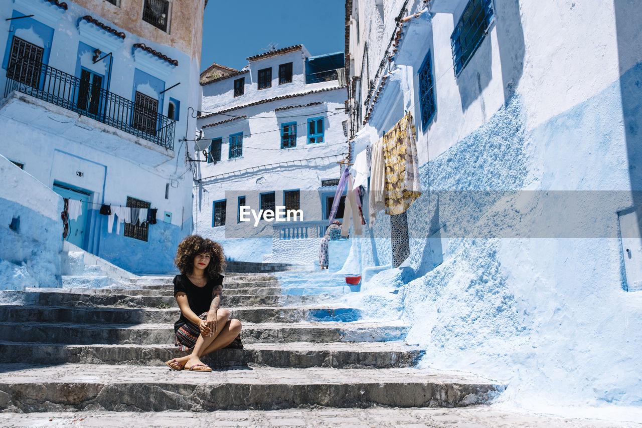 Portrait of woman sitting on staircase against buildings in city