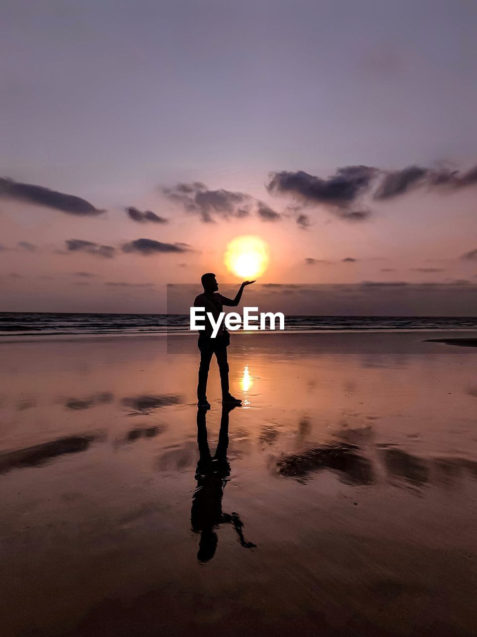 Optical illusion of silhouette man holding sun at beach during sunset