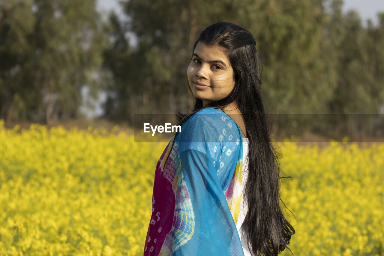 PORTRAIT OF SMILING YOUNG WOMAN STANDING ON LAND