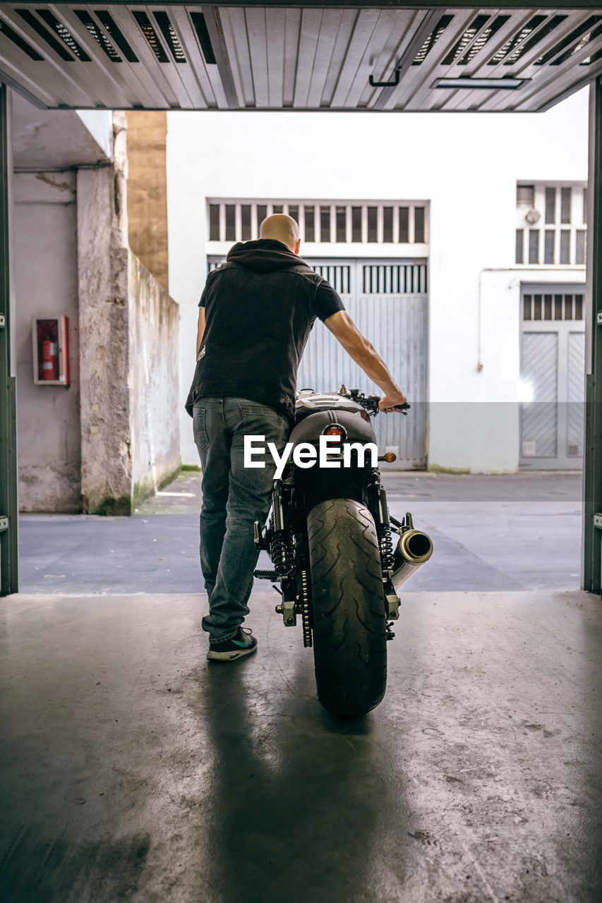 Rear view of man walking with motorcycle from garage