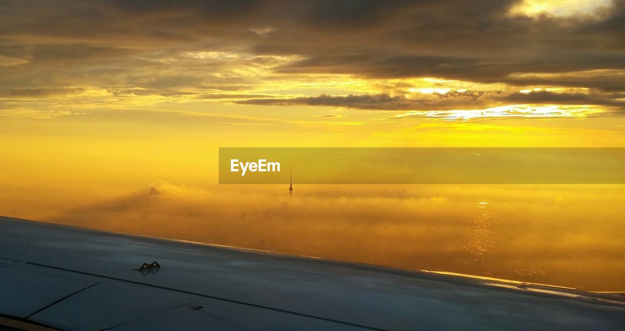 Cropped image of aircraft wing with fernsehturm amidst clouds