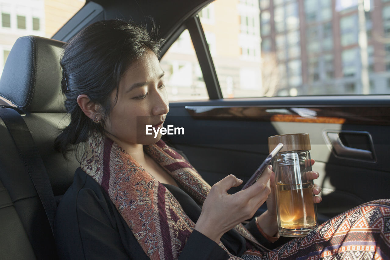 Young asian businesswoman looking at smartphone sitting in car service limousine