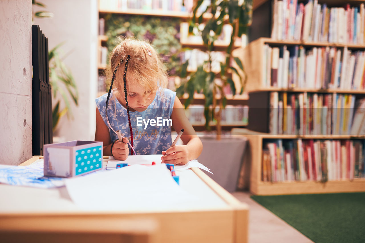 Schoolgirl doing homework. elementary student learning, drawing pictures, doing puzzles at desk