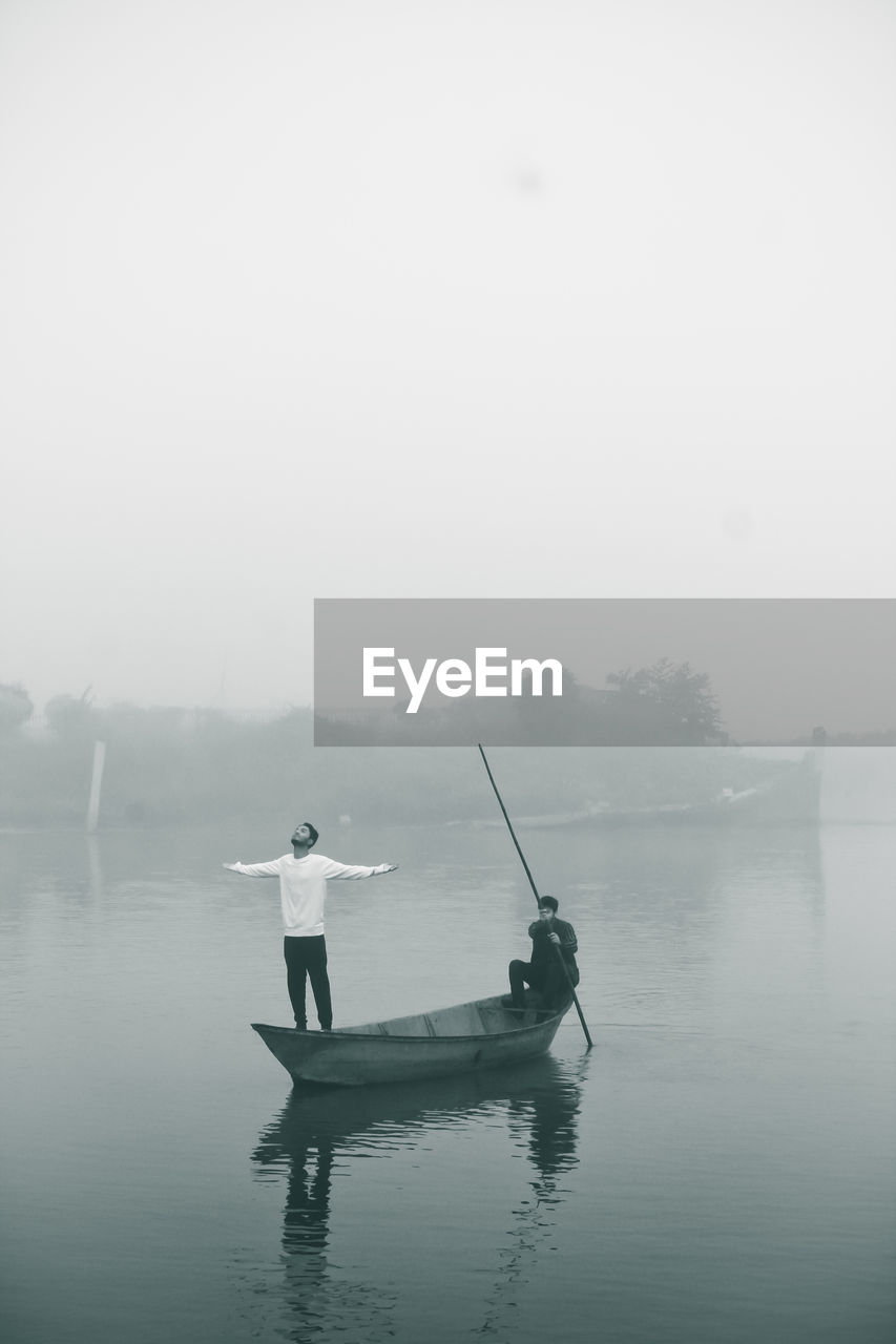 Men in boat on lake against sky during foggy weather