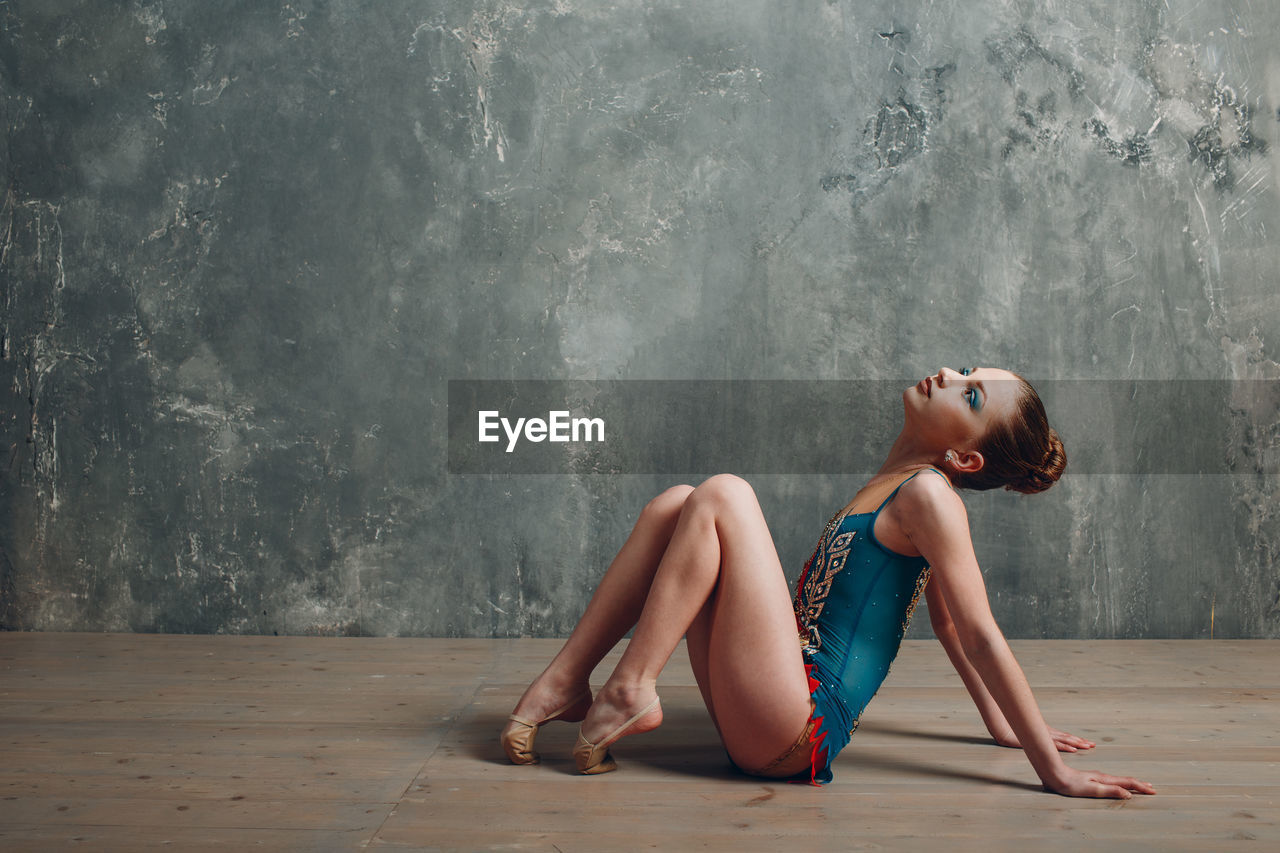 Gymnast girl sitting on hardwood floor against wall