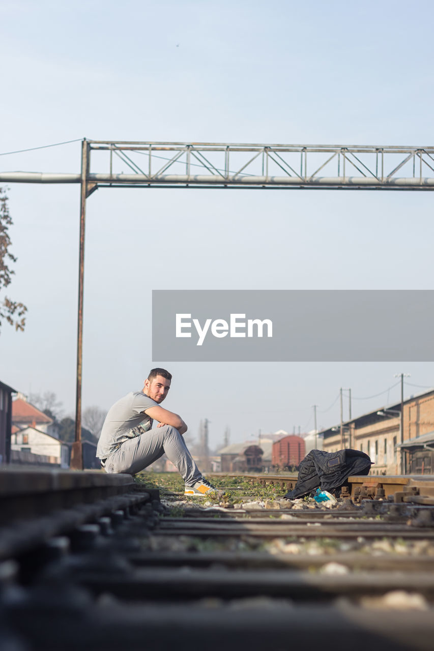 Side view of man sitting on railroad track in city