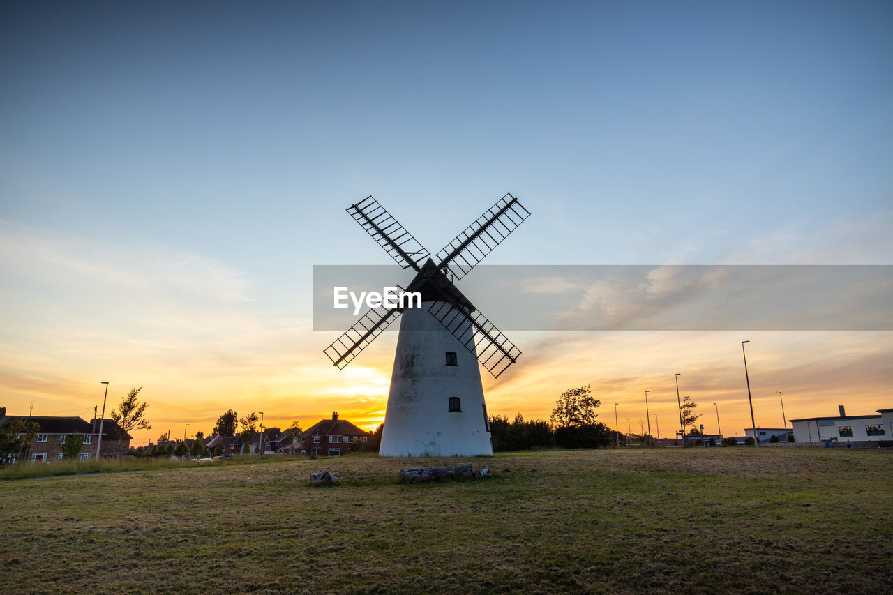 Traditional windmill on field against sky during sunset