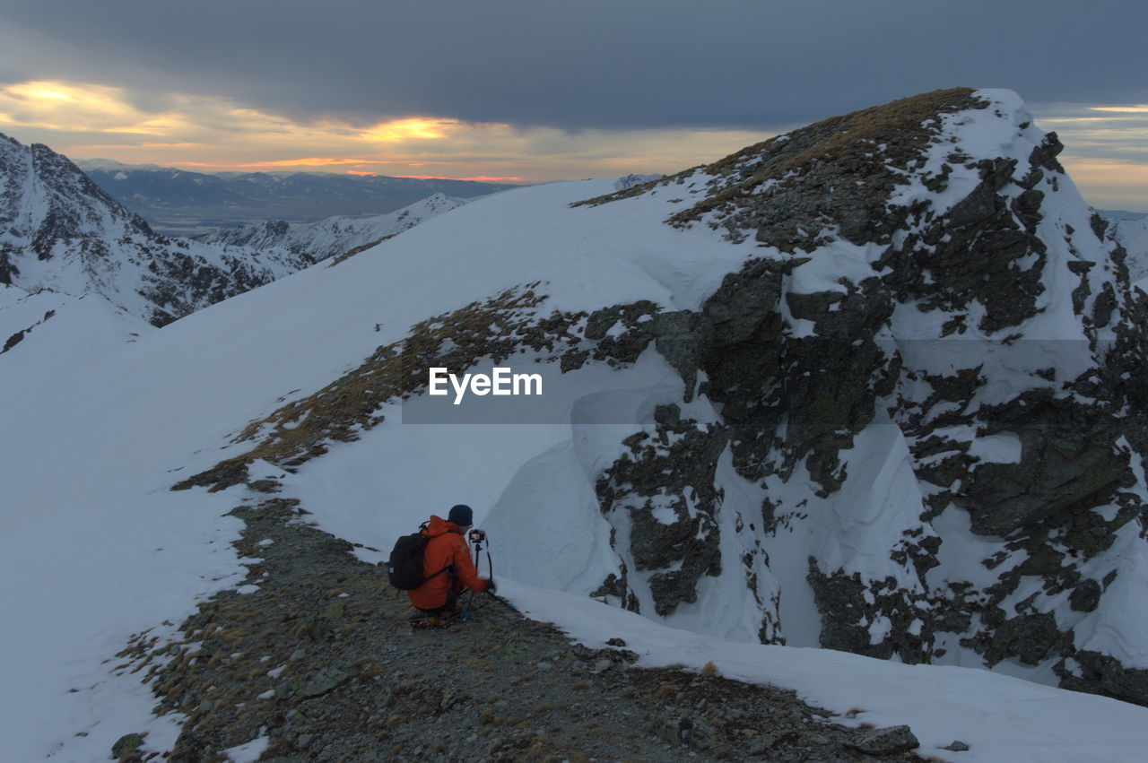 REAR VIEW OF PERSON ON SNOWCAPPED MOUNTAINS AGAINST SKY