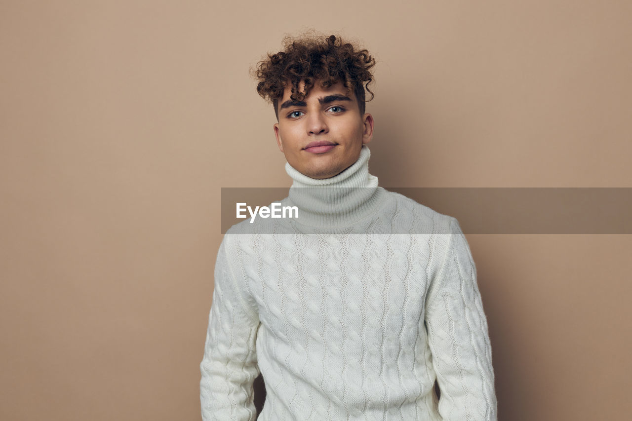 portrait, one person, studio shot, looking at camera, indoors, white, clothing, waist up, young adult, sleeve, fashion, front view, adult, curly hair, hairstyle, colored background, photo shoot, standing, individuality, serious, outerwear, copy space, brown hair, spring, person, casual clothing, human face, gray, sweater