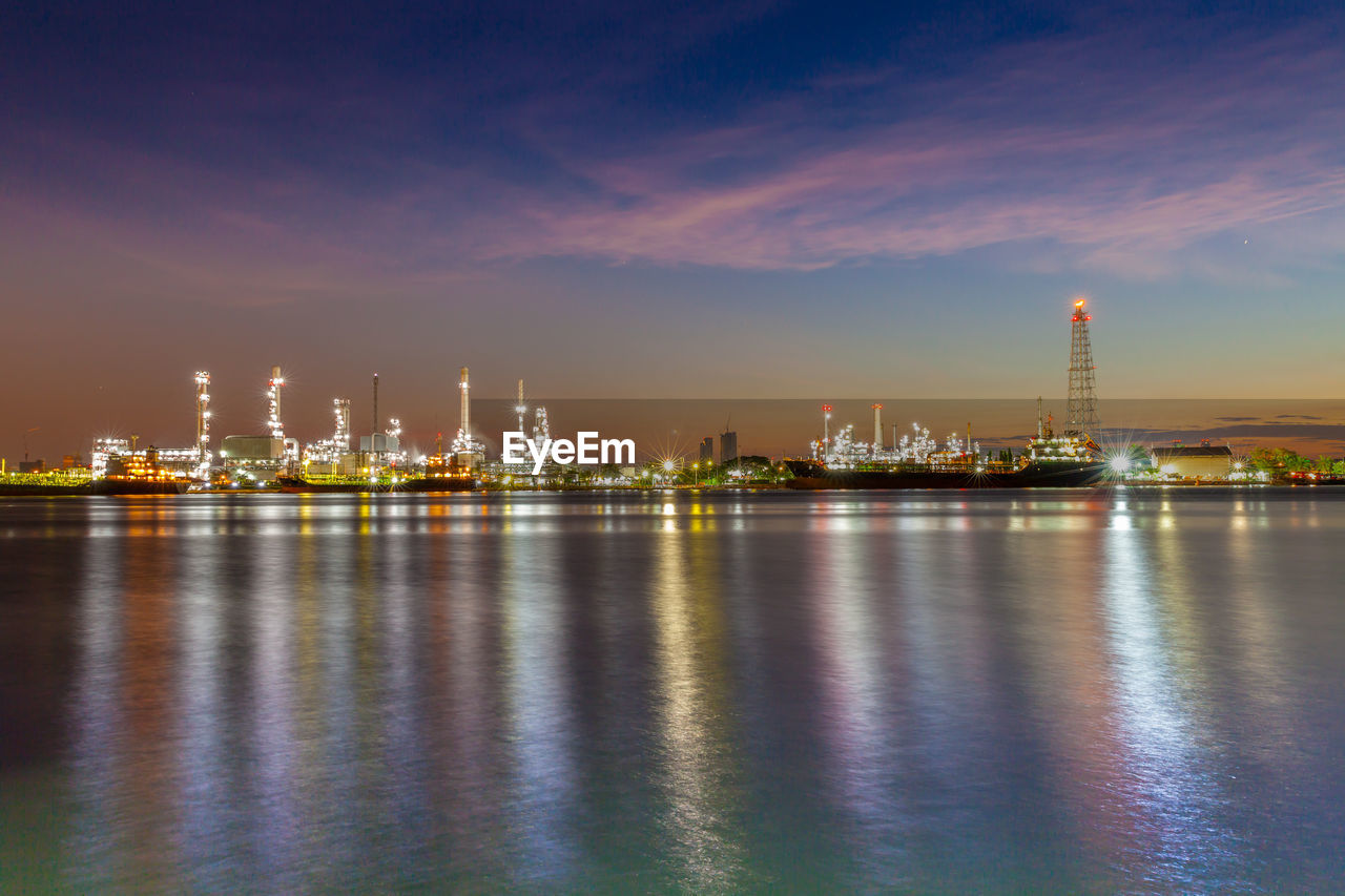 Illuminated city at waterfront during sunset