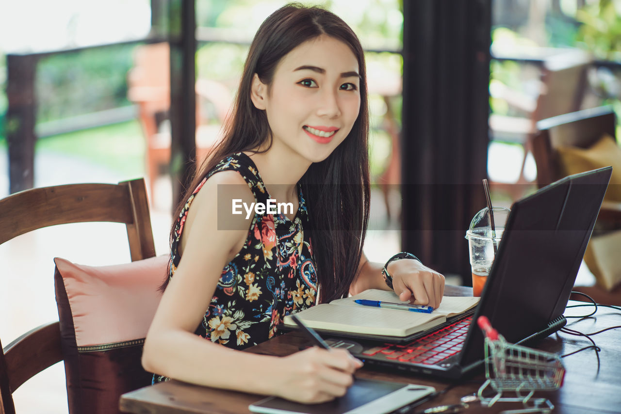 Portrait of smiling woman working with technologies while sitting on chair