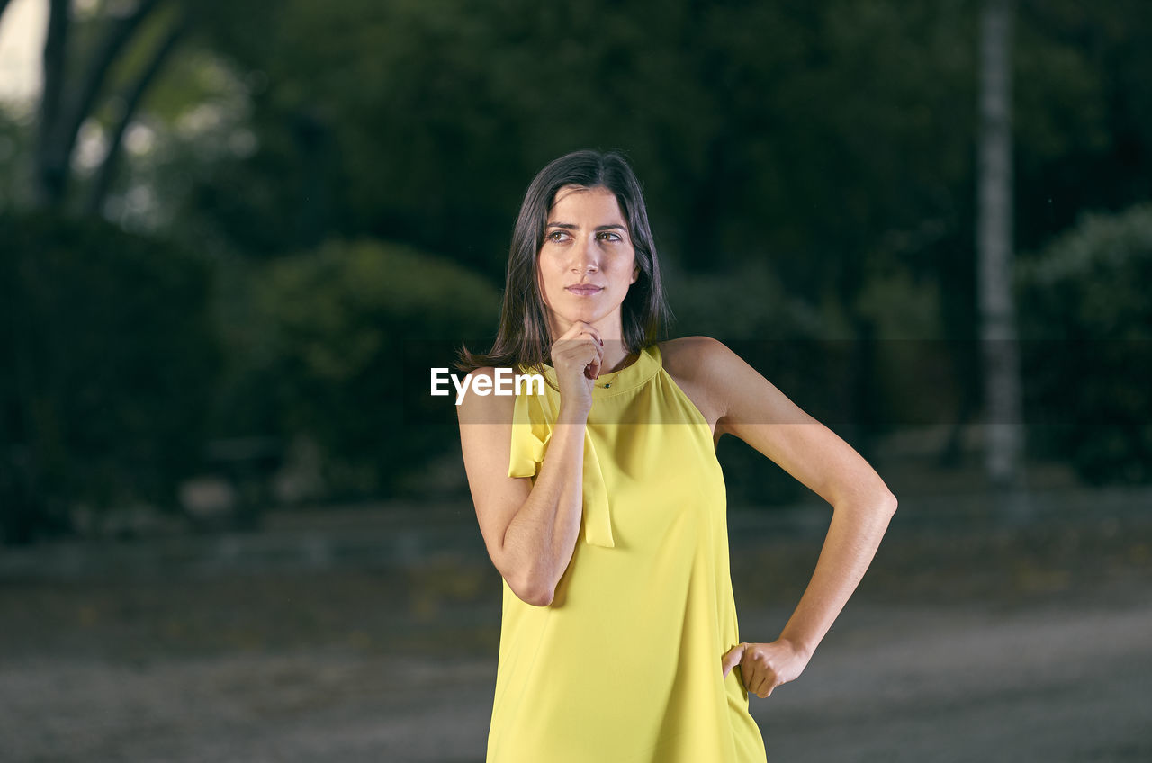 Thoughtful woman standing against trees on road