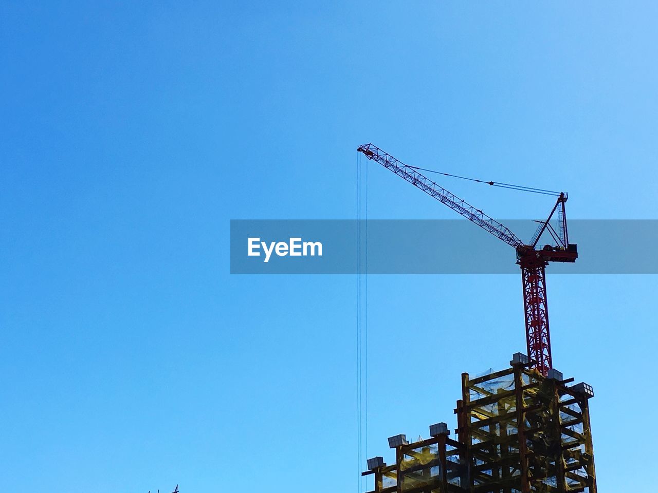 LOW ANGLE VIEW OF CRANES AT CONSTRUCTION SITE AGAINST CLEAR BLUE SKY