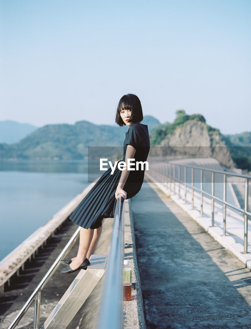 Woman sitting on walkway railing against clear sky