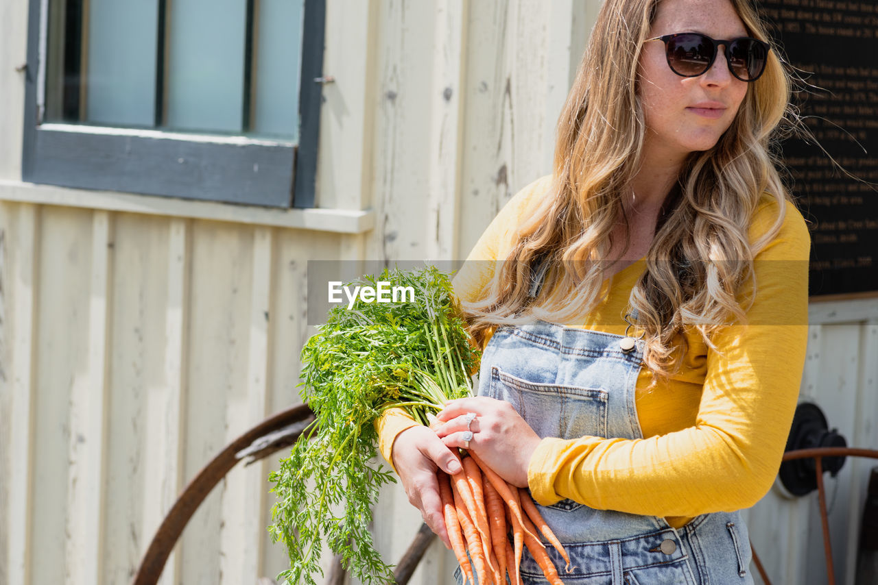 Beautiful woman holding carrots while standing outdoors