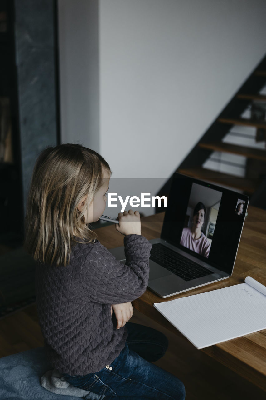 Girl attending class through video call on laptop at home