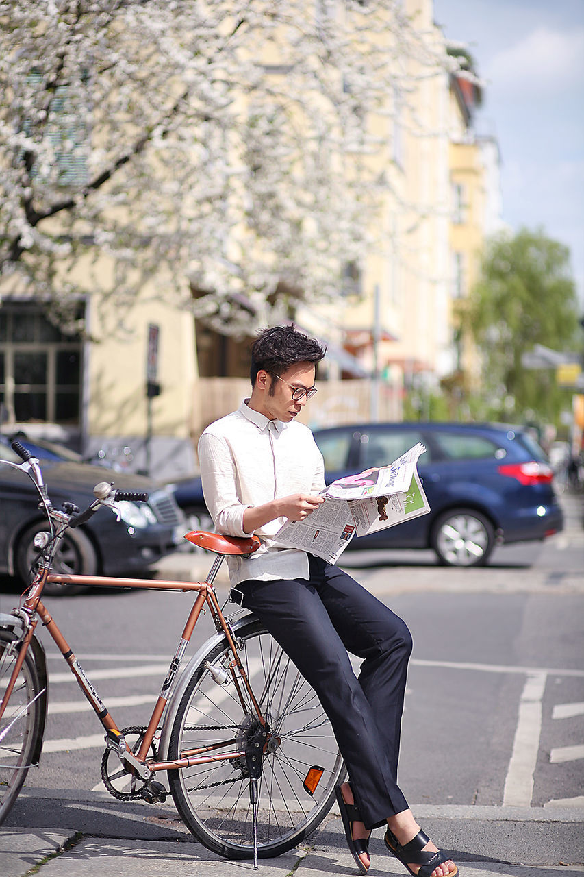 Young man sitting on bicycle while reading newspaper