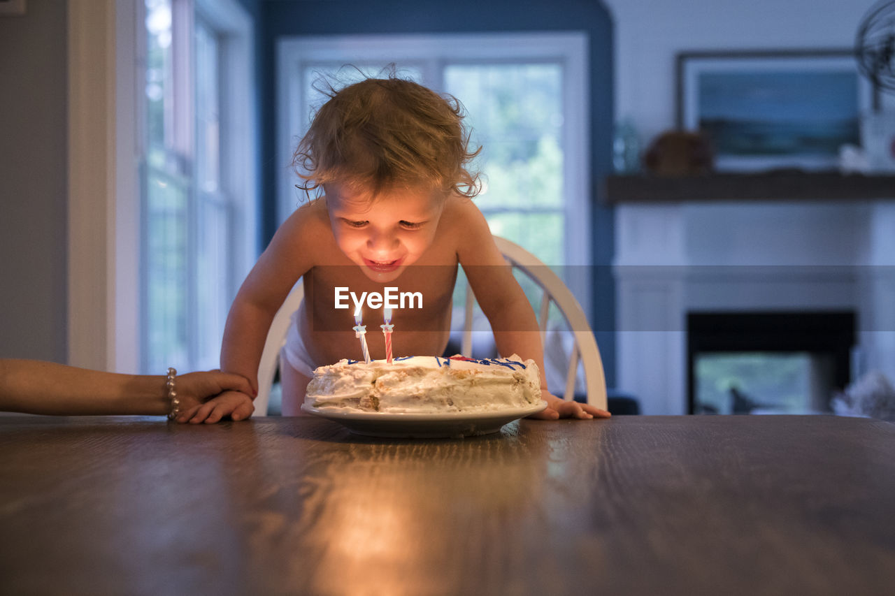 Candlelit toddler boy blowing out candles on birthday cake