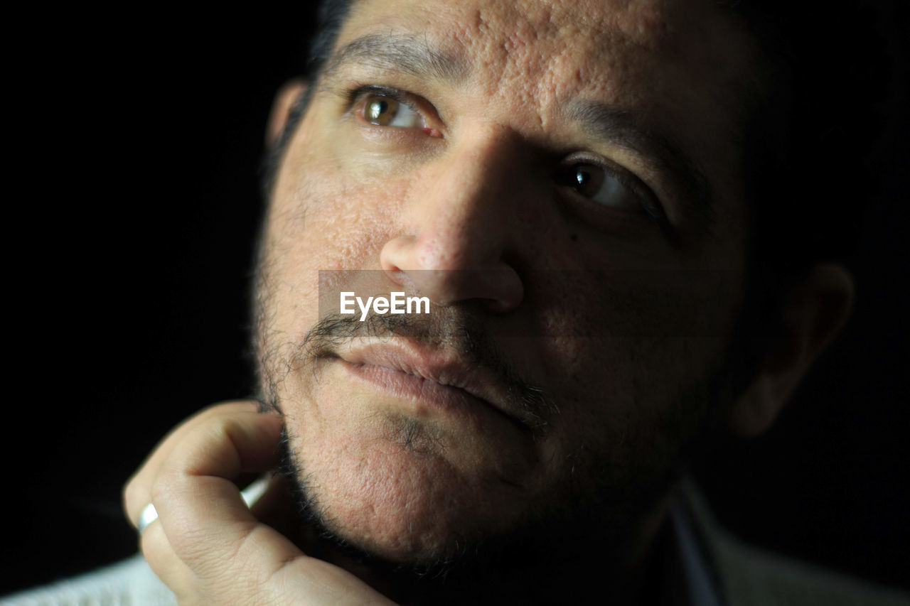 Close-up of thoughtful mid adult man looking away against black background