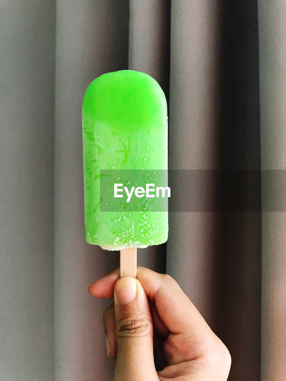 CLOSE-UP OF HAND HOLDING ICE CREAM CONE ON TABLE