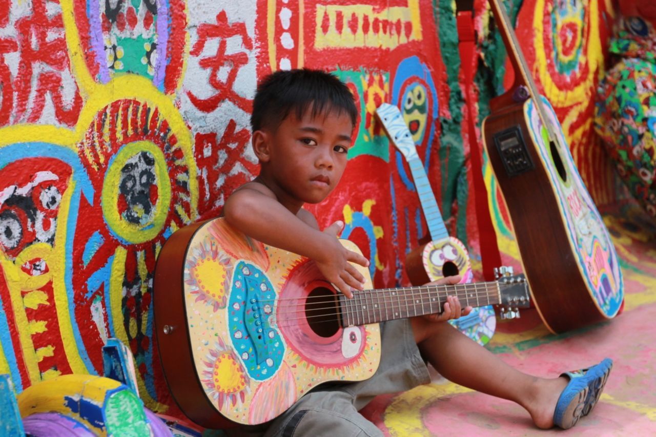 Portrait of little boy playing guitar against colorful wall