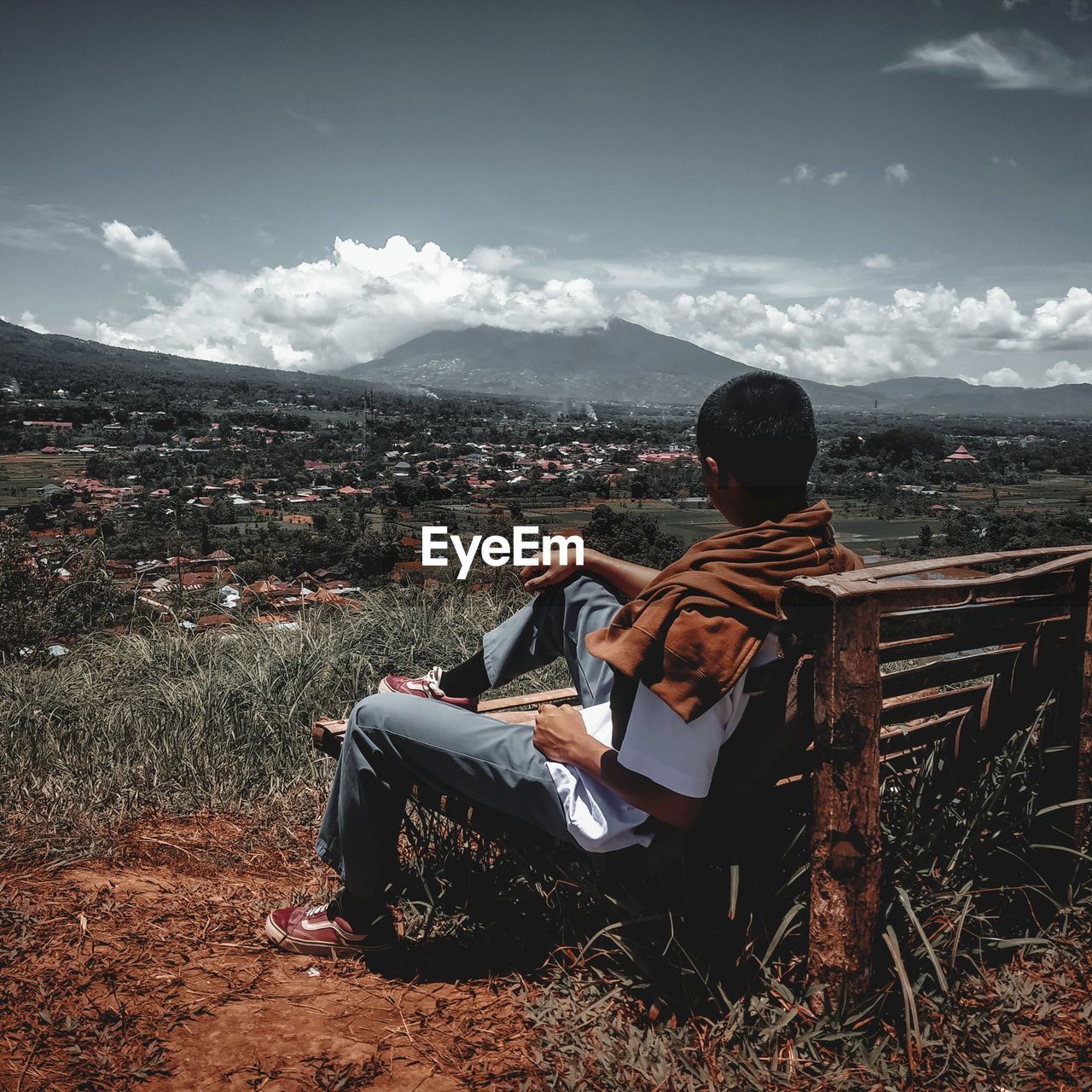 REAR VIEW OF MAN SITTING ON SEAT IN CITY