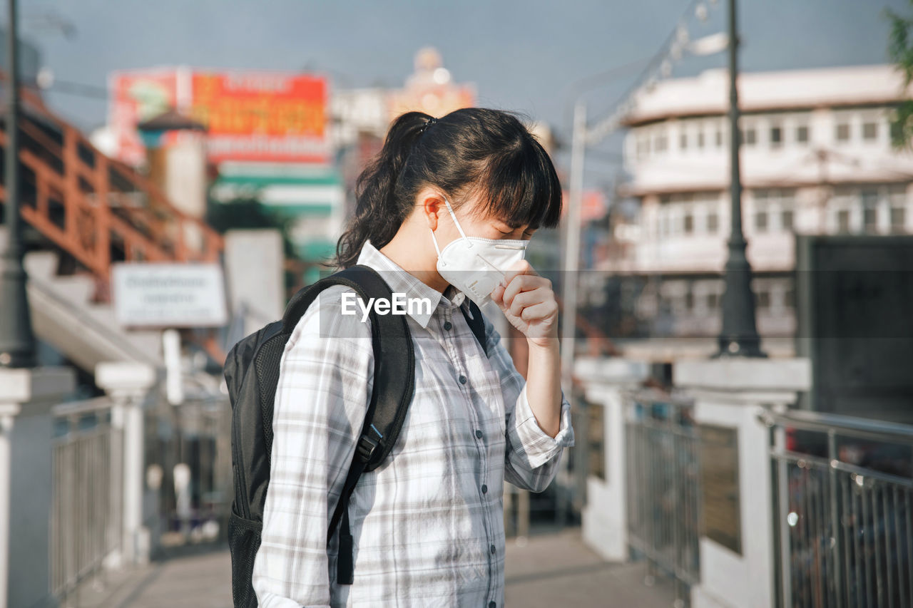 Woman wearing pollution mask while standing on footpath