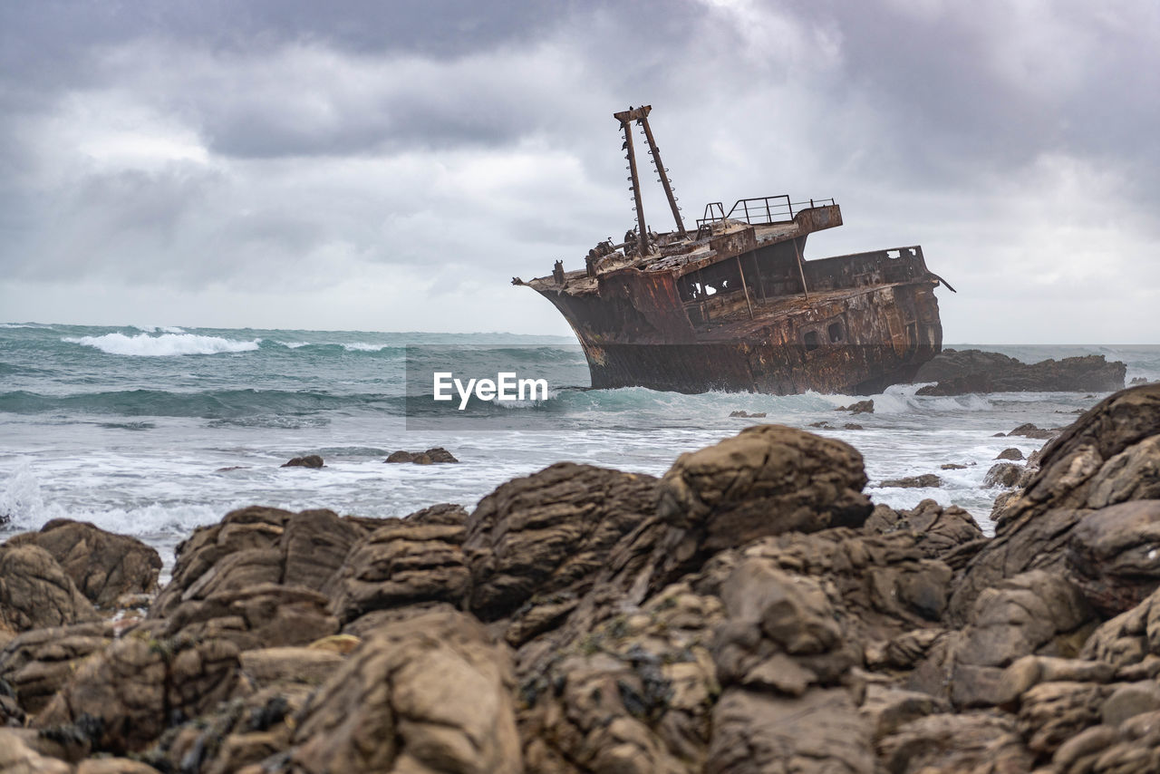 Shipwreck in sea against cloudy sky