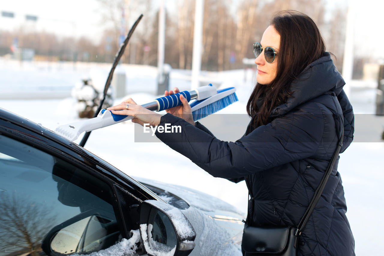 Woman cleans car with a brush from snow after a blizzard