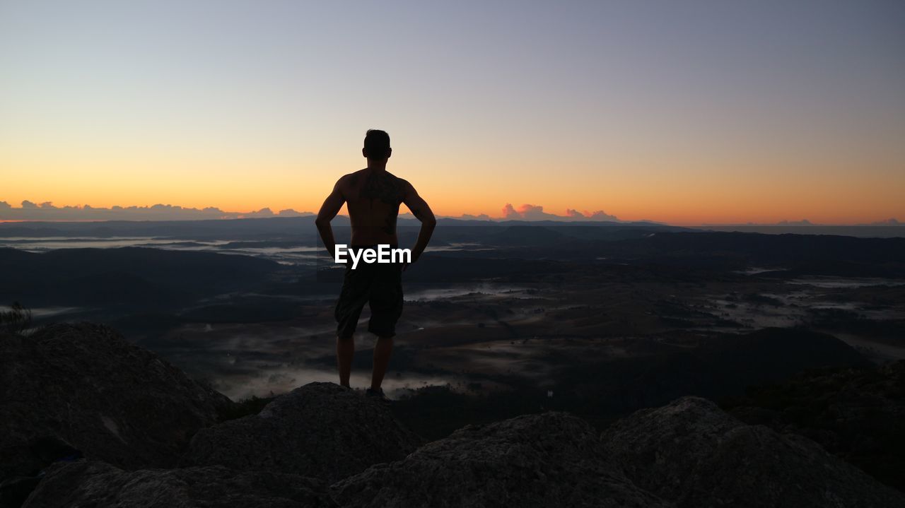 Man standing on rock against sky during sunset