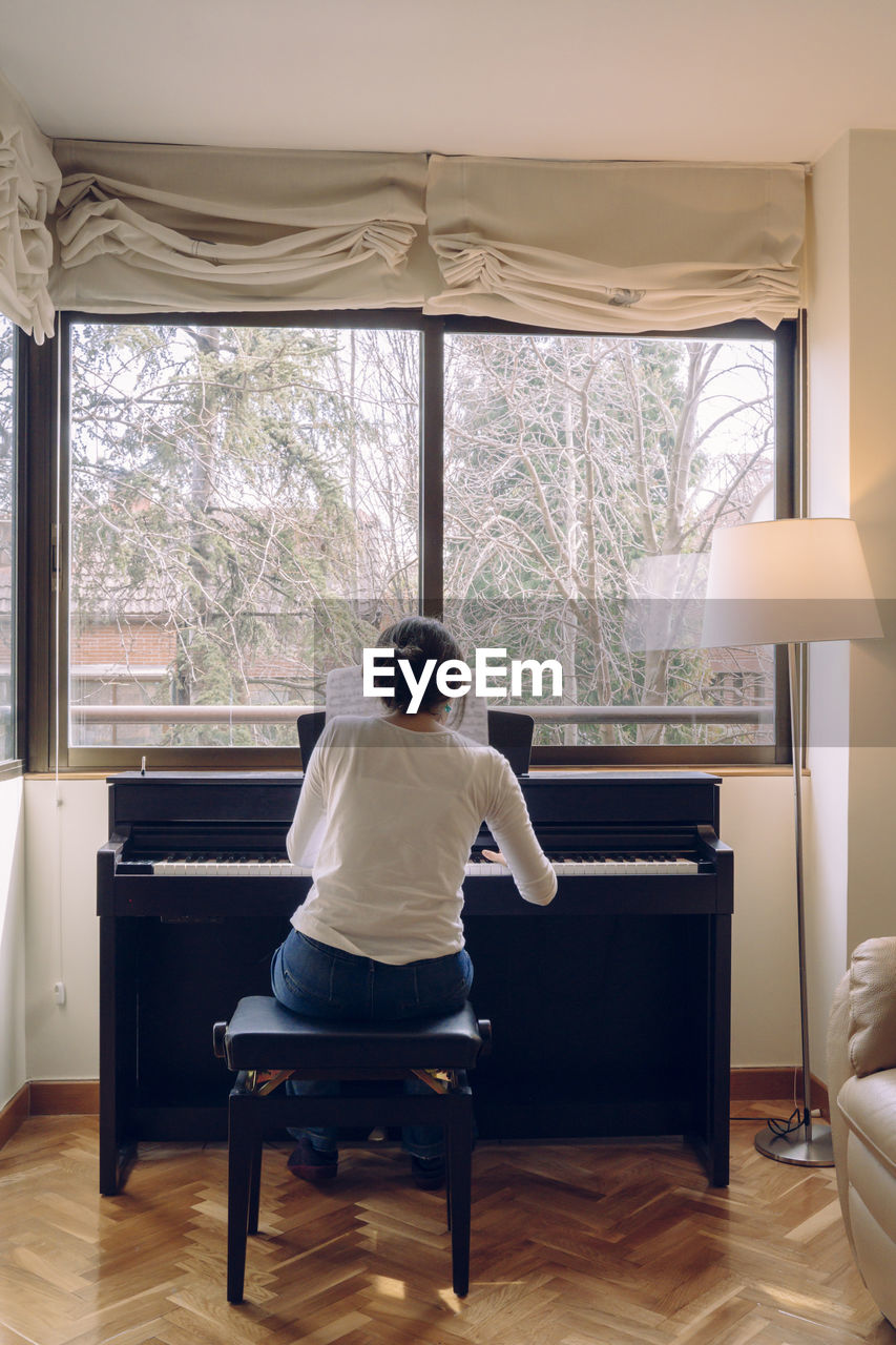 Rear view of woman playing piano while sitting on chair at home