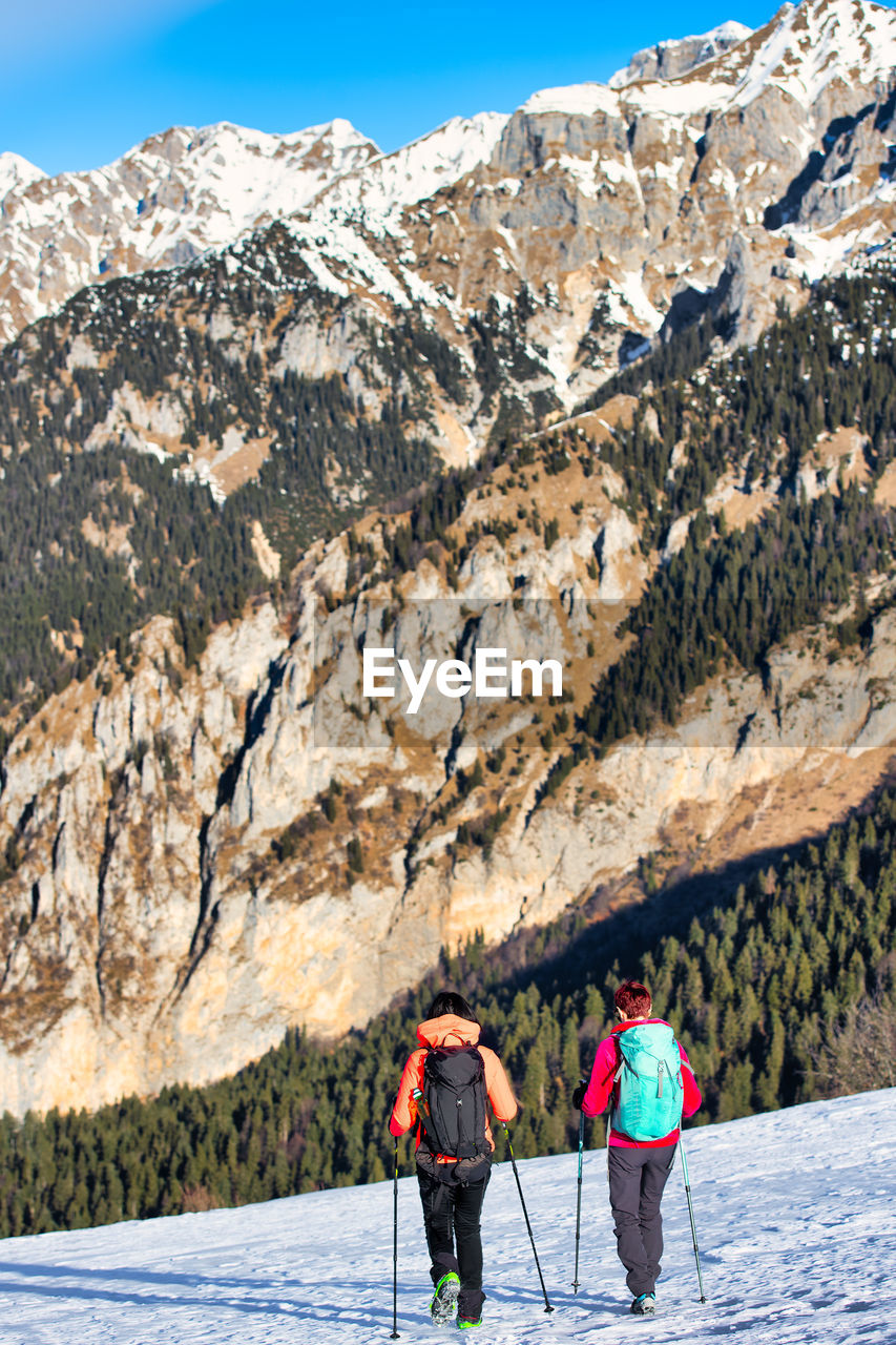 REAR VIEW OF PEOPLE WALKING ON ROCK AGAINST MOUNTAIN