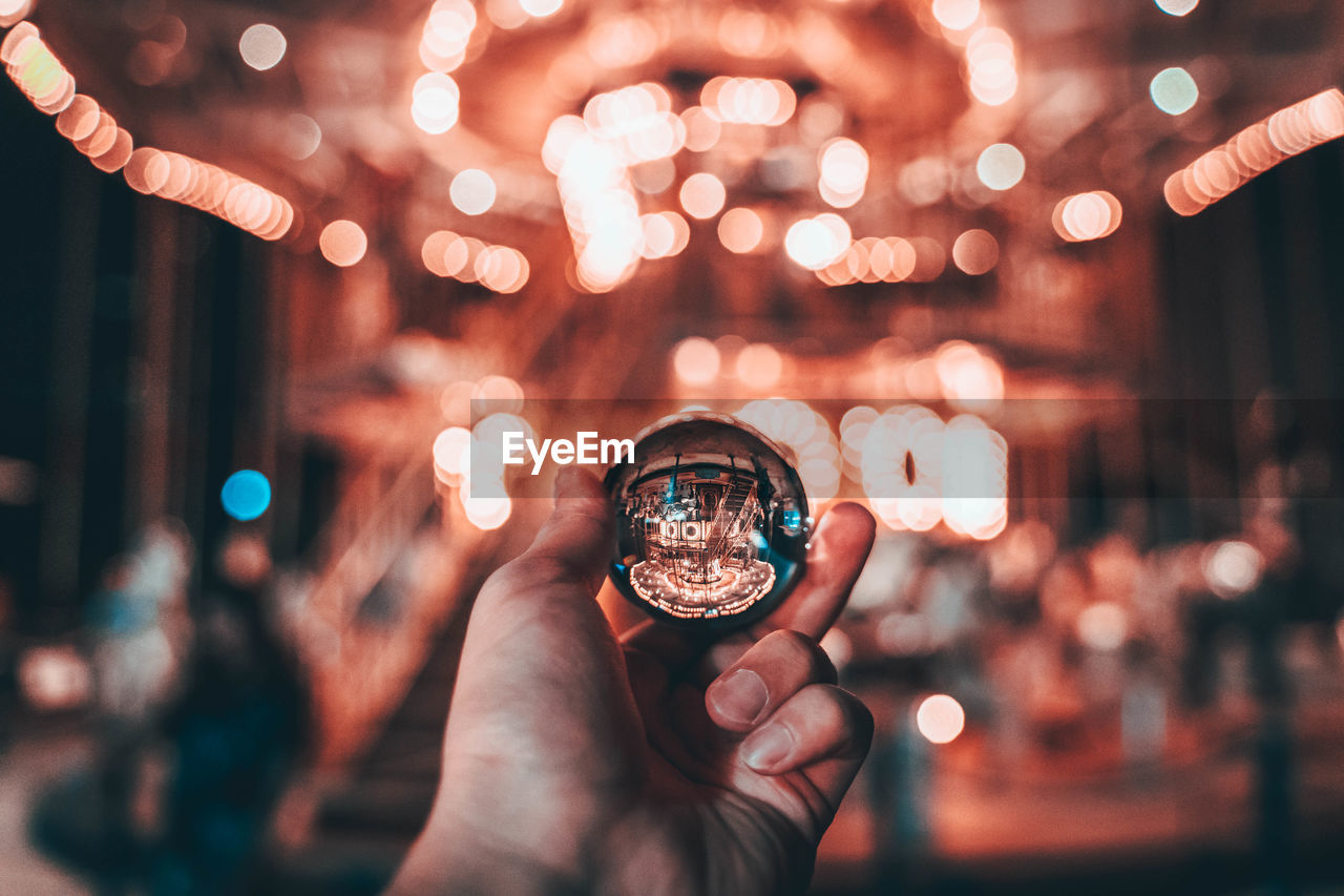 Close-up of hand holding crystal ball against illuminated amusement park ride